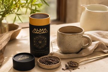 An open Alma Cacao canister with a measuring spoon, a dish of shaved cacao paste pieces and a warm mug, showing a single ceremonial cacao serving