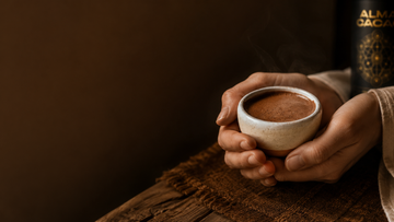Hands cradling a small ceramic bowl of thick, steaming ceremonial cacao on a rustic wooden table