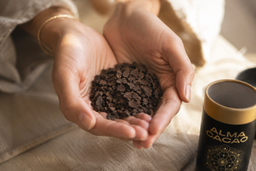 Two hands cupping shaved whole cacao paste pieces beside an Alma Cacao canister, the natural source of theobromine