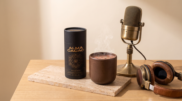 Alma Cacao canister and a steaming cup of ceremonial cacao beside a vintage podcast microphone and headphones