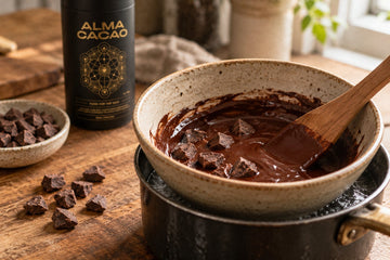 Whole cacao paste pieces melting in a stoneware bowl over a water bath beside the Alma Cacao canister, making chocolate without cacao powder