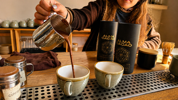 Ceremonial cacao being poured into ceramic cups beside two Alma Cacao canisters at The KINN elixir bar in Venice
