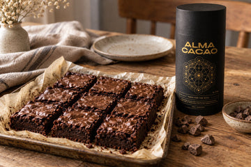 A tray of fudgy cacao paste brownies cut into squares beside small pieces of whole cacao paste on a wooden table.