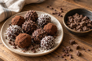 Hand rolled cacao truffles coated in nibs, coconut and cacao powder on a plate beside a bowl of whole cacao paste pieces