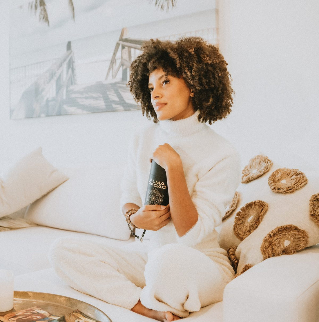 A woman relaxing on a white couch holding the Alma Cacao tin