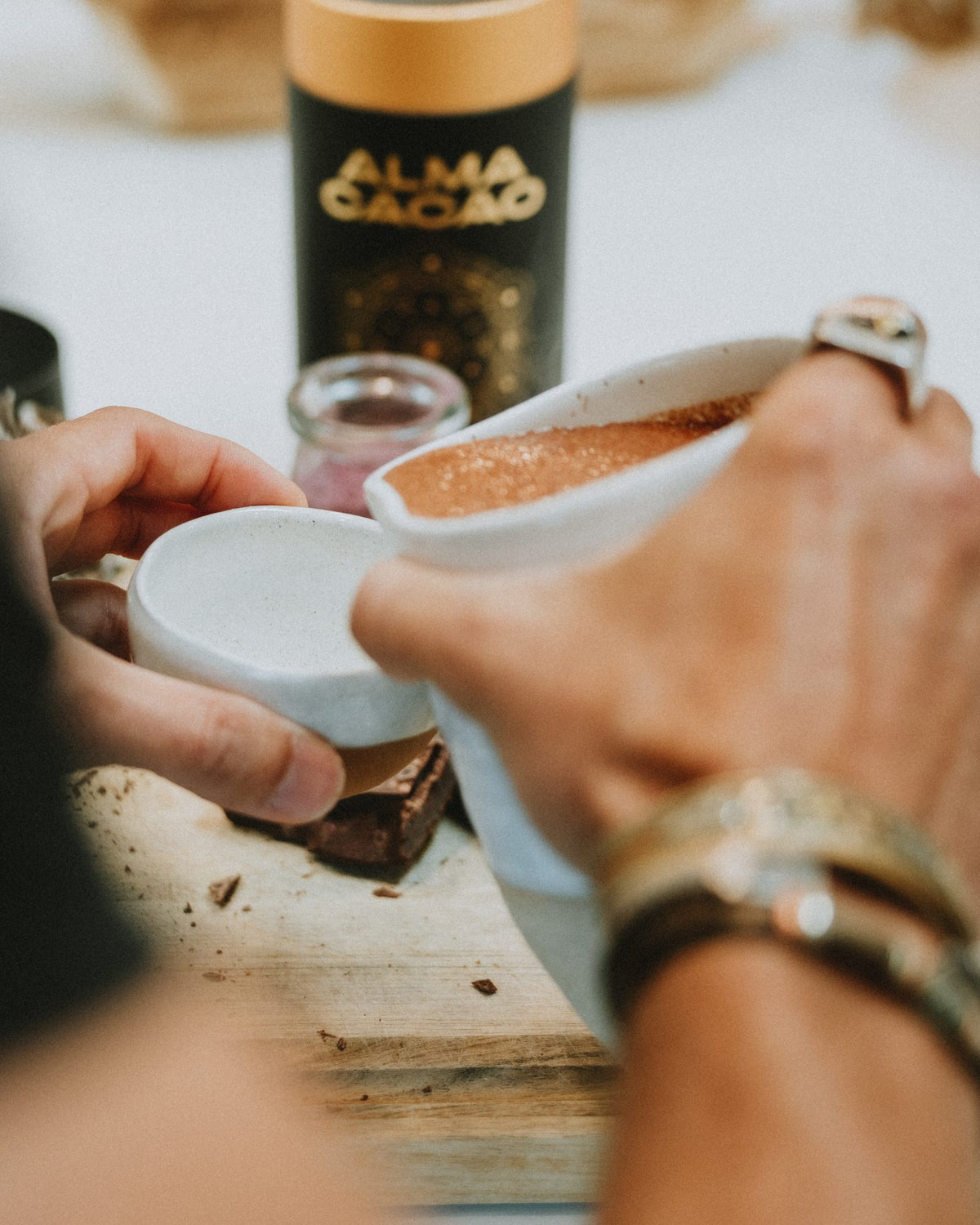 Serving ceremonial cacao from one cup to another, with the Alma Cacao canister behind